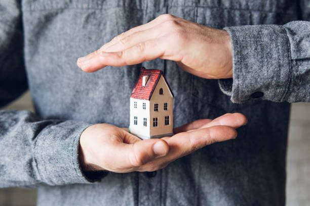 Hands holding and protecting small house. Conceptual image of insurance and staying home during Corona virus pandemic stock photo