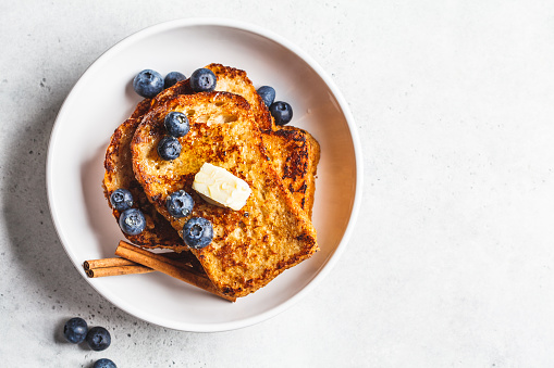 French toasts with blueberries and honey in a white plate.