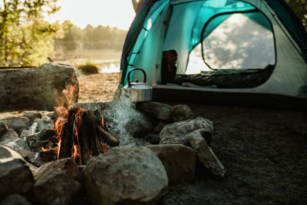 Campsite with tent and fire pit Campsite with a tent, kettle and burning fire pit in countryside. Camping by a lake in forest. camping stock pictures, royalty-free photos & images