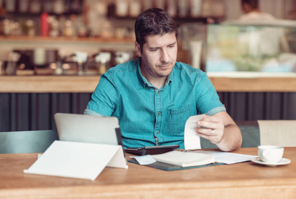 Entrepreneur managing his small business - Businessman looking overwhelmed - Young coffee shop owner going through paperwork stock photo