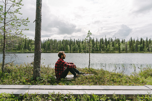 Young Caucasian man sitting in the forest near the river in Finland