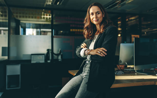 Mature businesswoman sitting on her desk Mature businesswoman sitting on her desk. Confident female entrepreneur with her arms crossed looking at camera. chief executive officer stock pictures, royalty-free photos & images