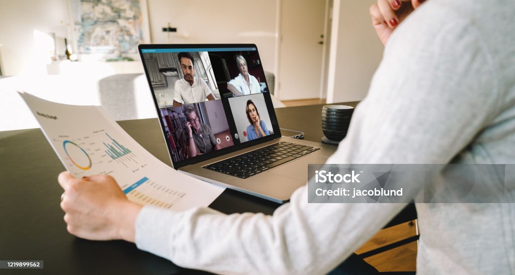 Business team in video conference Group of businessmen and businesswomen smart working from home. View from side of woman talking to her colleagues about business plan over a video conference. Telecommuting Stock Photo