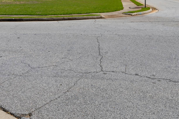 istock Cracked asphalt intersection with formed curbs and green grass border, aged and weathered street surface 1219901768