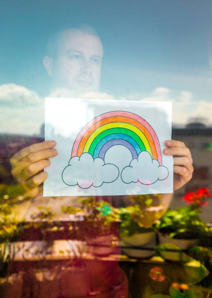 istock Man holding rainbow in window during Covid-19 pandemic 1219903191