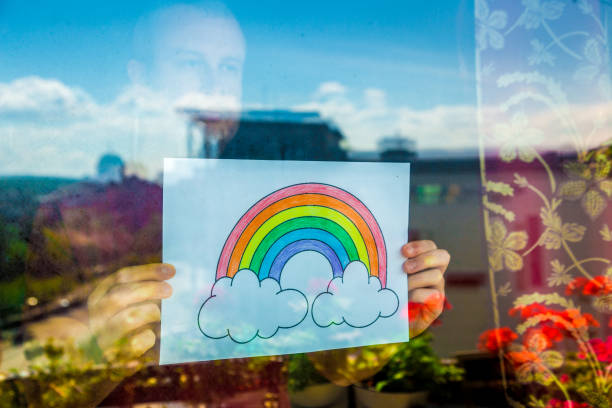 istock Man holding rainbow in window during Covid-19 pandemic 1219903192