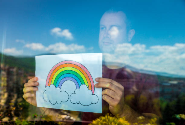 Man holding rainbow in window during Covid-19 pandemic
