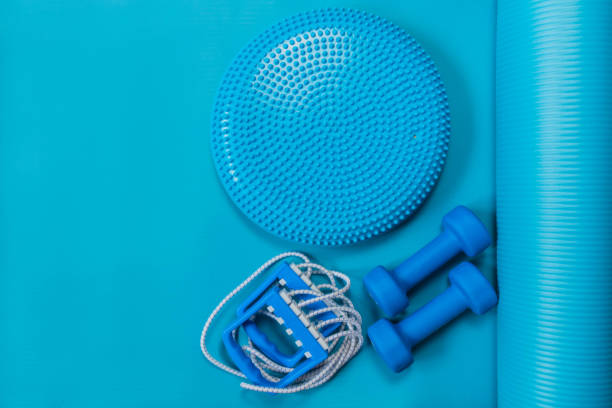 Fitness concept - blue dumbbells, expander and massage cushion on yoga mat stock photo