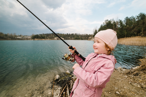 Little girl catching a fish. Lonely happy little child fishing from beach lake or pond with text space. Photo of children pulling rod while fishing on the weekend.
