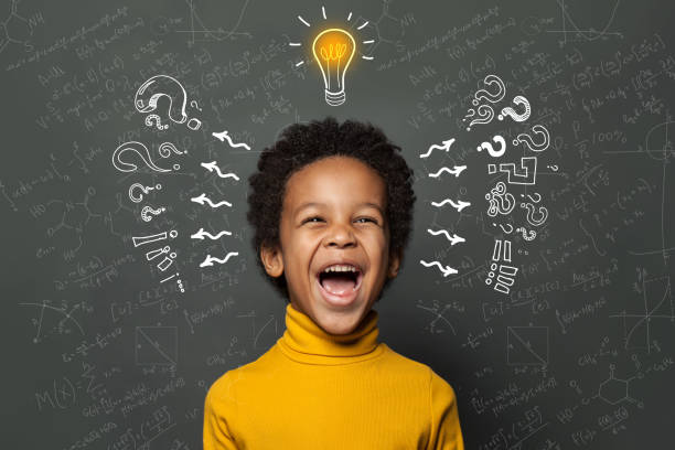 istock Smart black kid student with lightbulb on blackboard background. Brainstorming and idea concept 1219909786