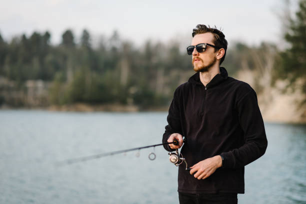 istock Fisherman with rod, spinning reel on the river bank. Man catching fish, pulling rod while fishing from lake or pond with text space at weekend. Fishing for pike, perch, carp on beach lake or pond. 1219911400