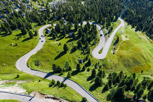 Aerial view of an alpine road surrounded by Italian alps and pine forest.