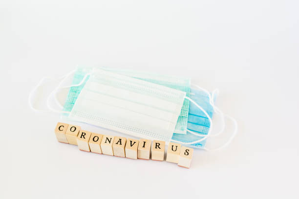 istock Word coronavirus written with wooden blocks with black letters isolated with a protective surgical mask 1219913376
