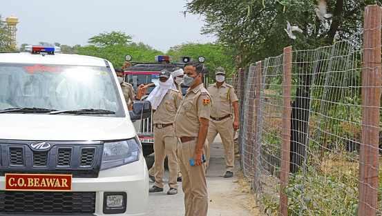 Beawar, Rajasthan, India - April 19, 2020: Policemen stands wearing protective face mask at Roopnagar village during first day of curfew imposed in 28 village after new case of COVID-19 in Beawar.