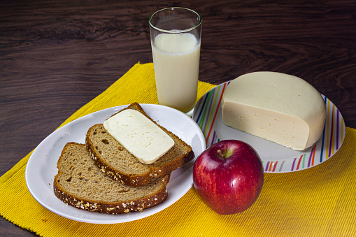 Brazilian breakfast with milk, cheese, loaf bread and apple in a dark wooden table. Health and fresh food