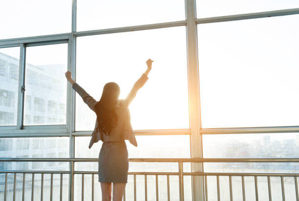 istock Businesswoman looking through the window with arms raised 1219916664