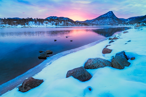 Beautiful soft colorful light coming over the mountain tops along Lake estes shoreline in a spring or winter morning