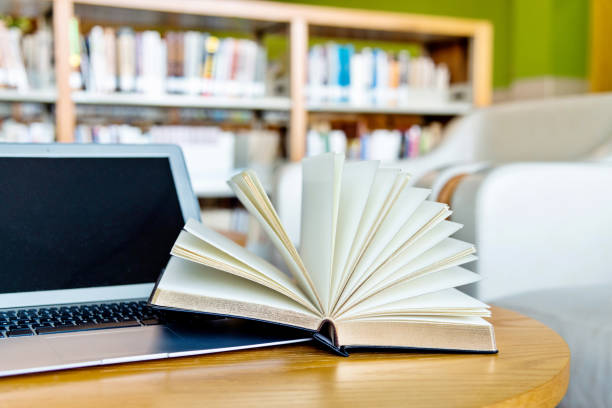 istock Laptop and open book on the table of public library 1219922389