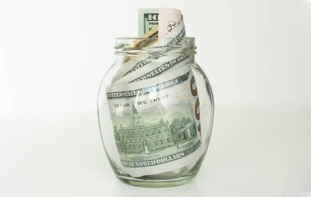 istock Many 100 US dollars bank notes in a glass jar isolated on white background 1219923594