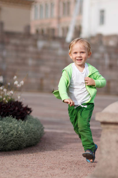 uma criança loira de aparência européia com roupas verdes feliz corre ao longo da praça do senado em helsinque, na finlândia. - beautiful outdoors vertical close up - fotografias e filmes do acervo