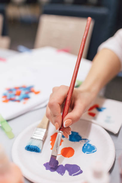 istock artist's hand dips a brush into a palette with purple colour. close-up 1219923953