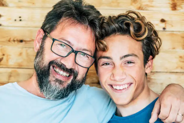 Cheerful people portrait with father and son hug and laughing a lot together having fun and looking at the camera - wooden background and joyful generations concept-handsome young and old males