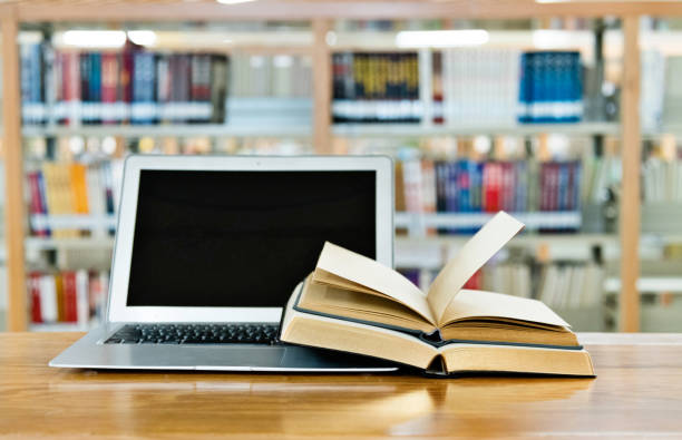istock Laptop and open books on the table of public library 1219924030