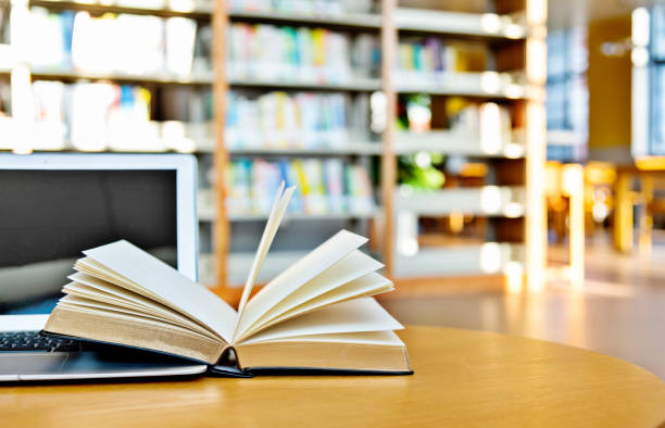 laptop and open book on the table of public library - applied science imagens e fotografias de stock