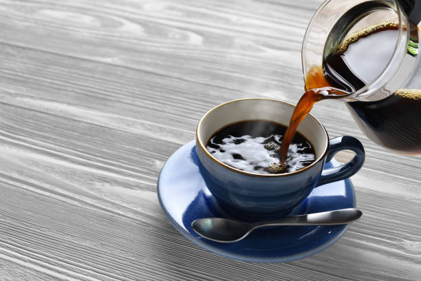 istock Pouring coffee with smoke on a cup on wooden background 1219924888