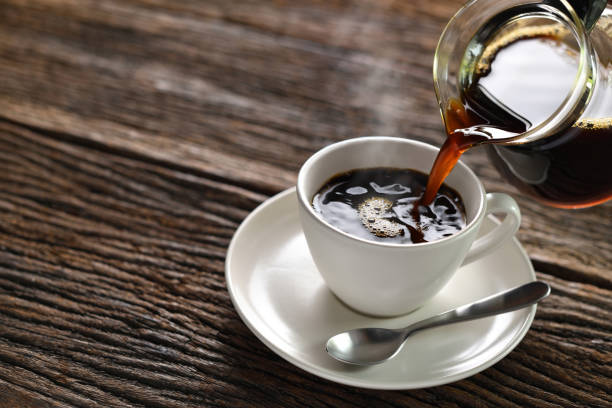 istock Pouring coffee with smoke on a cup on wooden background 1219924904