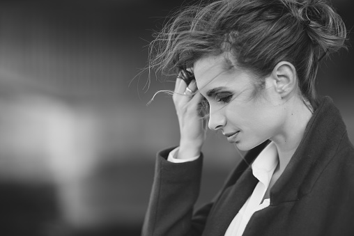 Beautiful lonely woman in a coat and scarf with her hair developing in the wind under a bridge on a cold gray day. The concept of loneliness. Black and white art photo. Soft selective focus.