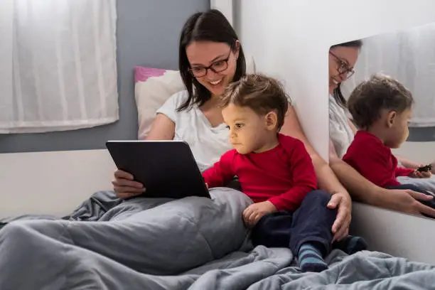Mother and toddler son with tablet in bed