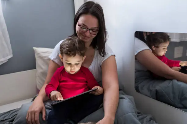 Mother and toddler son with tablet in bed