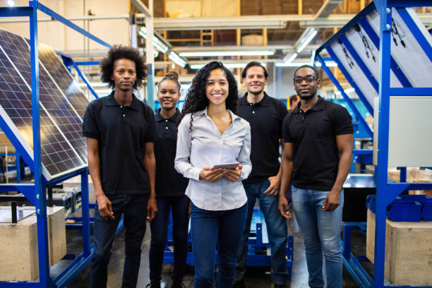 Group of solar panel factory employees standing together Multi-ethnic group of warehouse workers looking at camera and smiling. Group of employees standing together on solar panel factory shop floor. solar panel manufacturing stock pictures, royalty-free photos & images