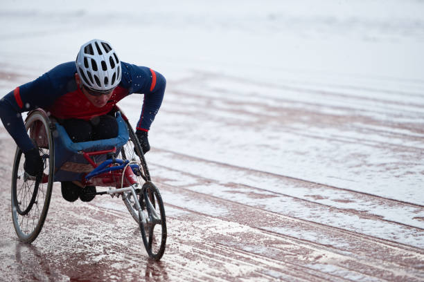 Wheelchair racing. Physically impaired male athlete in helmet training Wheelchair racing. Physically impaired male athlete in helmet training in racing wheelchair on track covered with melting snow in nasty wintry weather athlete with disabilities photos stock pictures, royalty-free photos & images