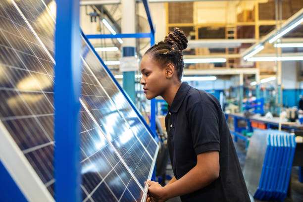 Quality engineer examining solar panels in factory Side view of a female employee inspecting newly manufactured solar panels in company. Woman quality engineer examining solar panels in factory. solar panel manufacturing stock pictures, royalty-free photos & images