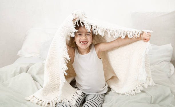 istock Cute little girl playing in bed with a blanket. 1219934529