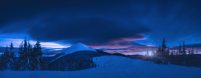 Alpine mountain valley covered with snow in a moonlight. Majestic winter night landscape.