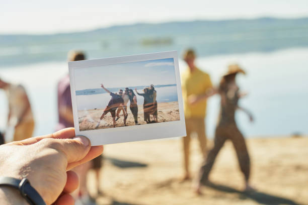 Summer Photo Of Friends Having Fun Close-up view of male hand holding polaroid photo print with young people hanging out on lake on beautiful summer day instant camera photos stock pictures, royalty-free photos & images