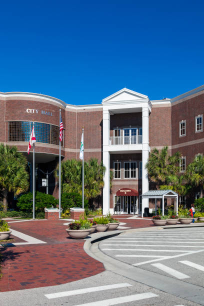 istock St Cloud Florida City Hall entrance with brick sidewalks, palm trees, Flag Poles and protective flower pots in front all under a perfect blue sky. 1219941432