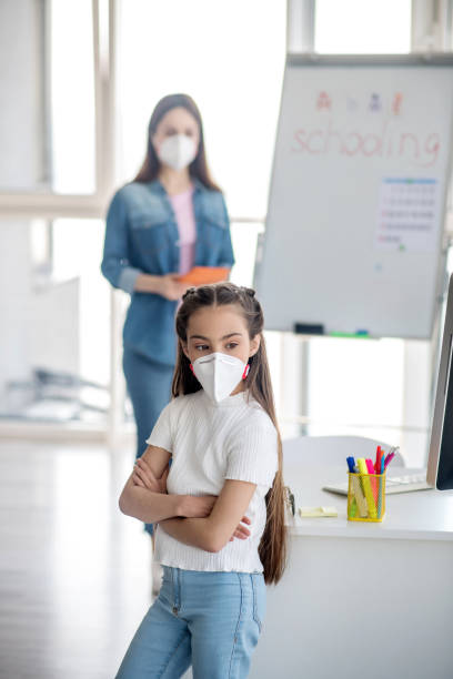 istock Little schoolgirl in protective mask standing clasped hands on her chest. 1219942621