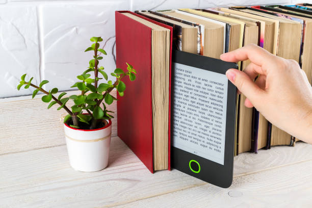 woman hand takes e-reader from shelf with paper books and small potted plant. copy space on e-book display. e-reading for pleasure and education. - kindle e reader book reading imagens e fotografias de stock