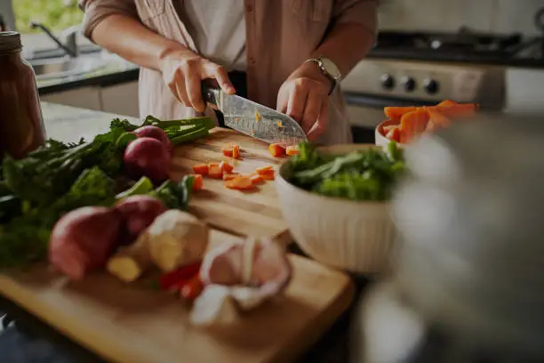 Photo of Closeup of young female hands chopping fresh vegetables on chopping board while in modern kitchen - preparing a healthy meal to boost immune system and fight off coronavirus