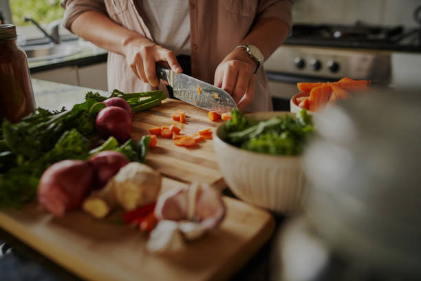 closeup of young female hands chopping fresh vegetables on chopping board while in modern kitchen - preparing a healthy meal to boost immune system and fight off coronavirus - healthy food imagens e fotografias de stock