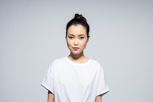 Portrait of beautiful asian young woman wearing white t-shirt, looking at camera. Studio shot, grey background.