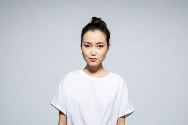 Beautiful young woman on grey background Portrait of beautiful asian young woman wearing white t-shirt, looking at camera. Studio shot, grey background. central asian ethnicity stock pictures, royalty-free photos & images