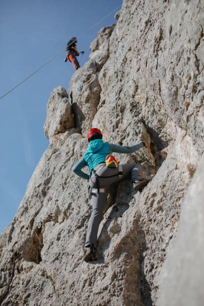 istock Woman rock climbing while belayer controls the rope that is attached to the climber 1219945894