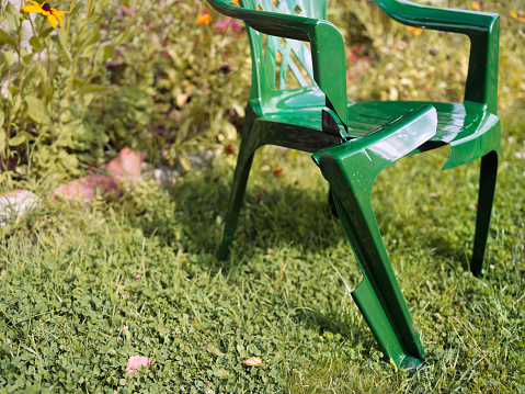 Plastic garden chair with broken leg, summertime shot with lush plants in the background