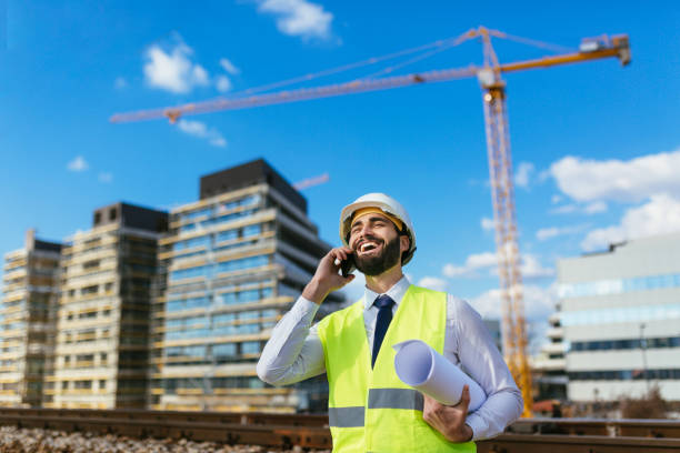 istock Cheerful engineer holding blueprint and talking on mobile phone on construciton site 1219949809