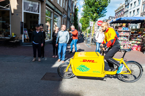 Young man on delivery bicycle circulating in Amsterdam, Netherlands Amsterdam, Netherlands - September 7, 2018: Young man on delivery bicycle DHL circulating and people walking in an old historic center of Amsterdam, Netherlands cargo bike photos stock pictures, royalty-free photos & images